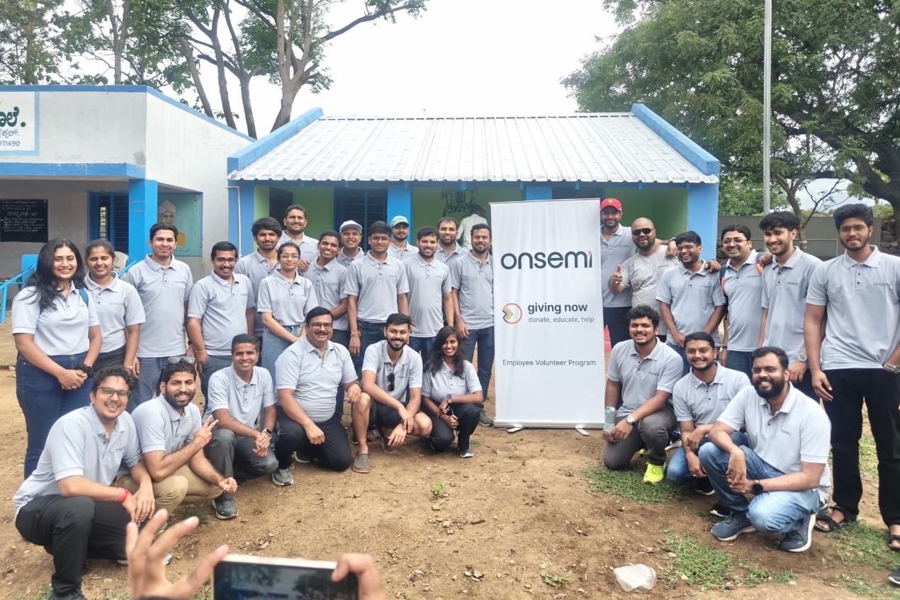 A group of onsemi employee volunteers gather outdoors for a team photo beside a Giving Now Employee Volunteer Program banner at a community service project site.