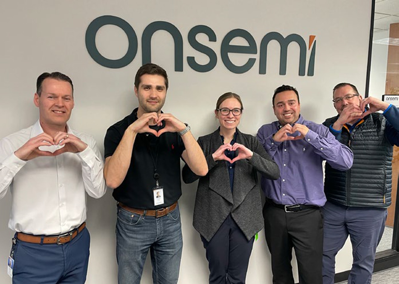 Two ladies standing by the onsemi logo, forming a heart shape with their hands.