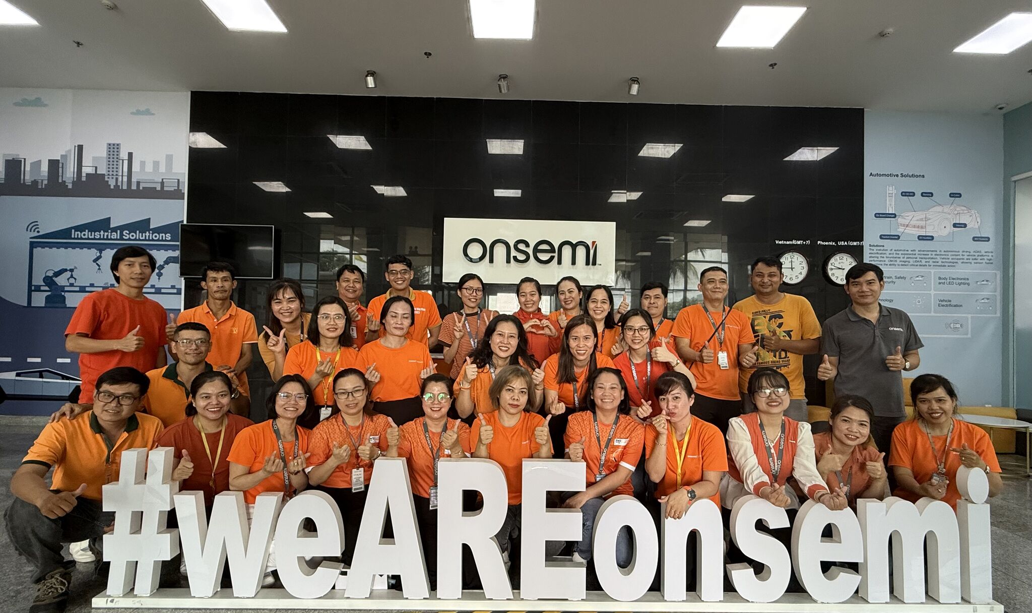 Two ladies standing by the onsemi logo, forming a heart shape with their hands.